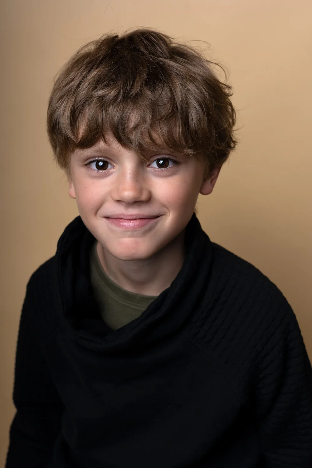 Portrait d’un petit garçon en pull noir, sur fond beige.