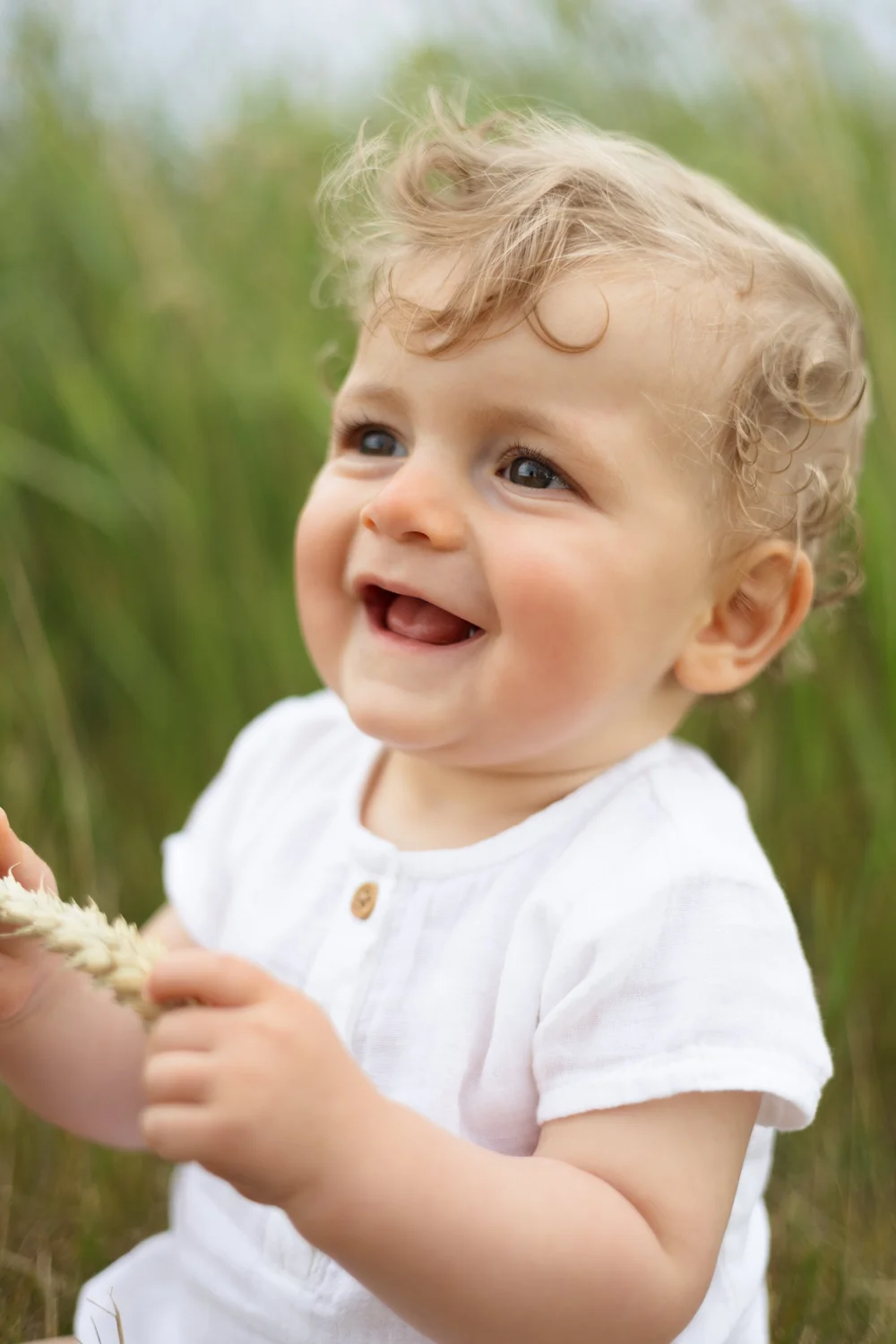 Bébé souriant en chemise blanche dans les hautes herbes.