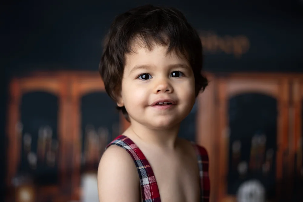 Portrait d’un petit garçon en chemise à carreaux, sur fond sombre.