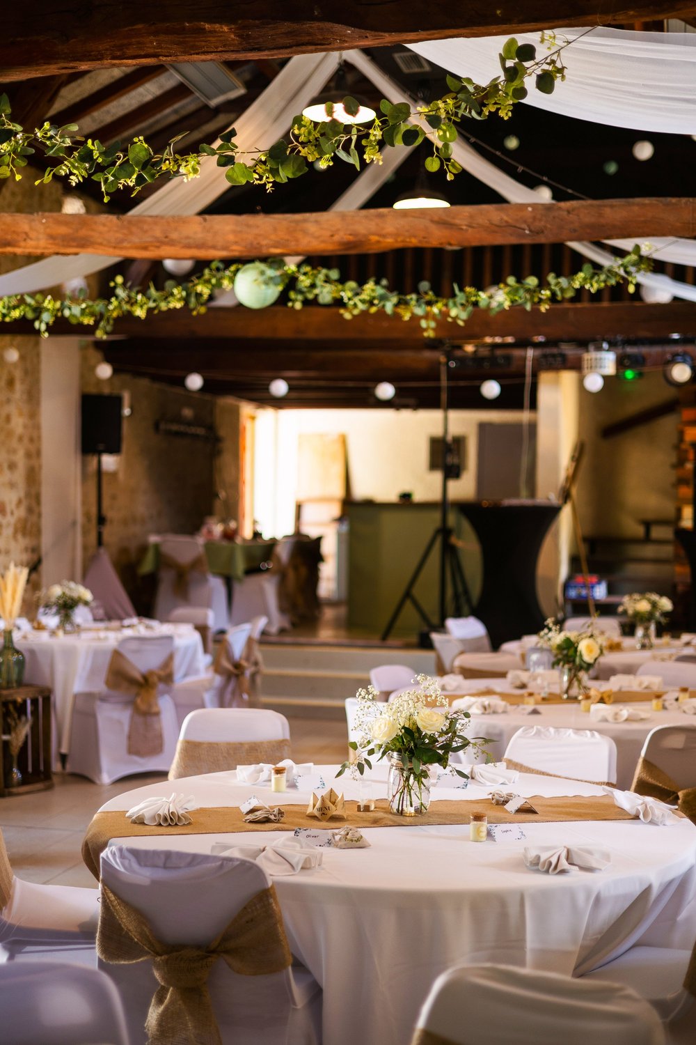 Salle de réception décorée de guirlandes de feuillage et tables rondes.