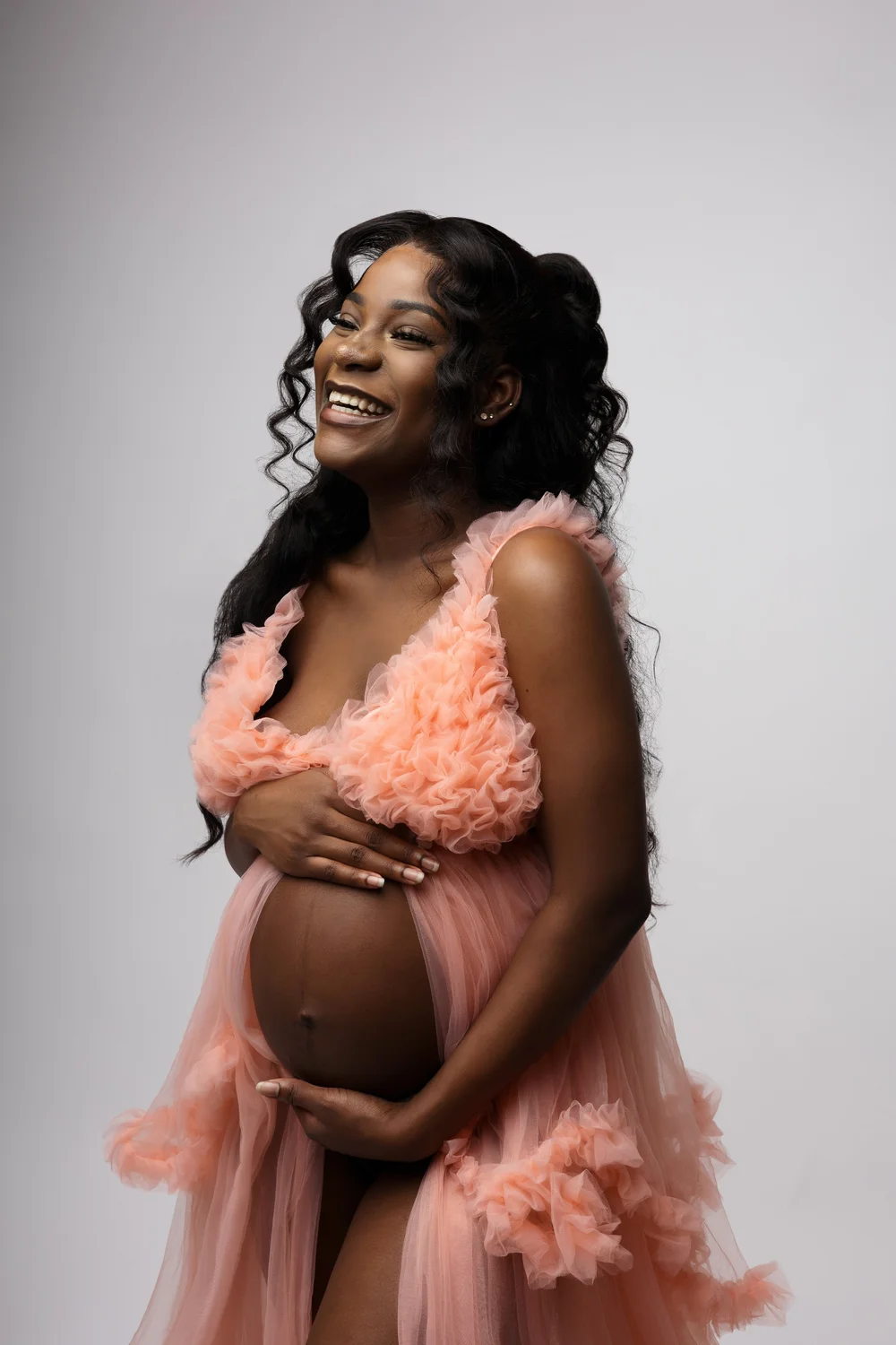 Femme enceinte en robe rose vaporeuse, sur fond clair.
