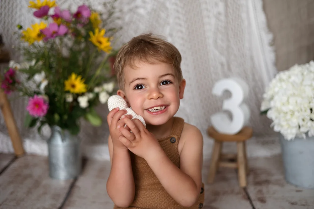 Petit garçon souriant près d’un bouquet et d’un chiffre 3.