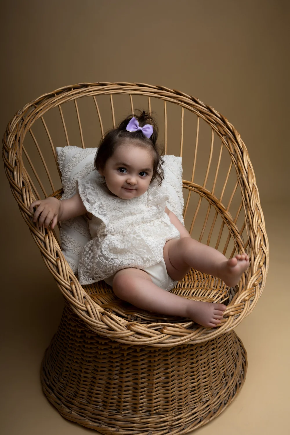 Bébé en robe de dentelle assise dans un fauteuil en rotin.