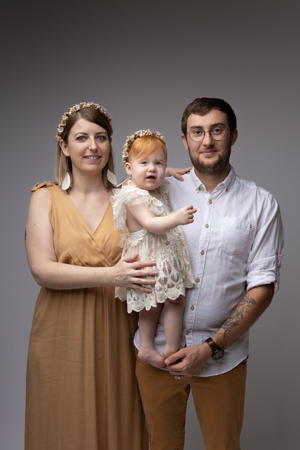 Parents en studio tenant leur bébé, couronnes de fleurs.