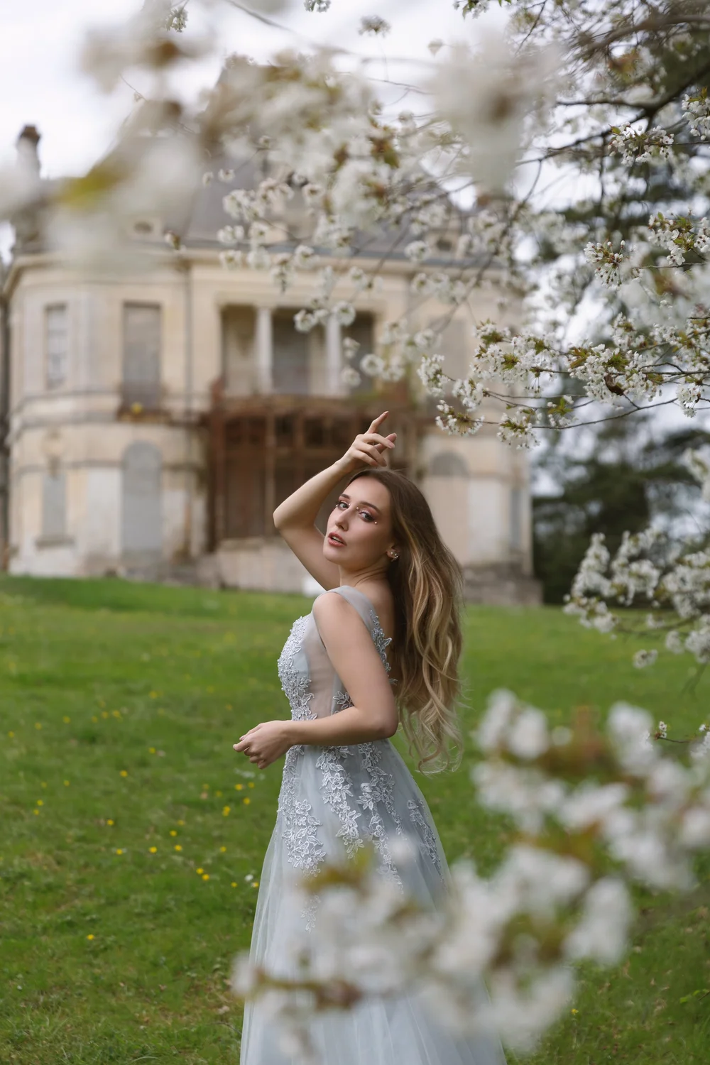 Femme en robe bleue devant une vieille demeure, derrière des fleurs de cerisier.