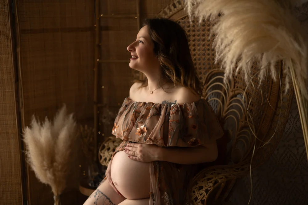 Femme enceinte en robe fleurie devant un paravent en rotin.