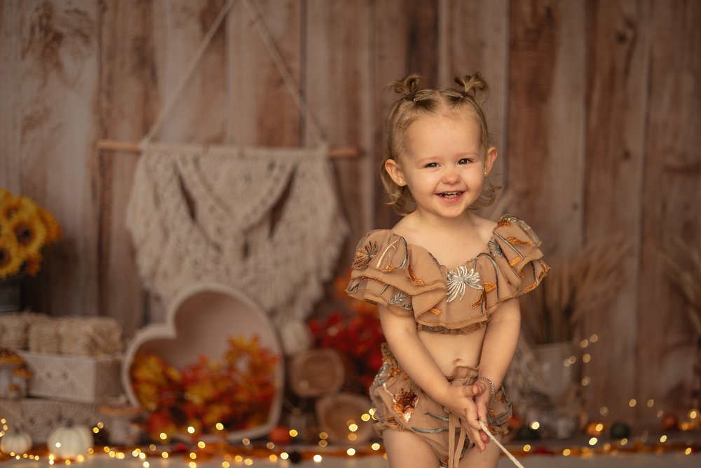 Bébé en robe beige devant un décor en bois et macramé, pour son anniversaire.