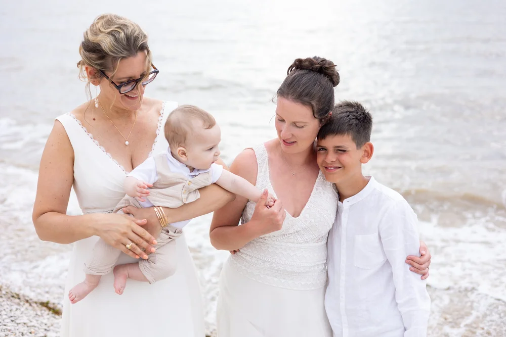 Deux mariées en robes blanches avec leurs enfants au bord de la mer.