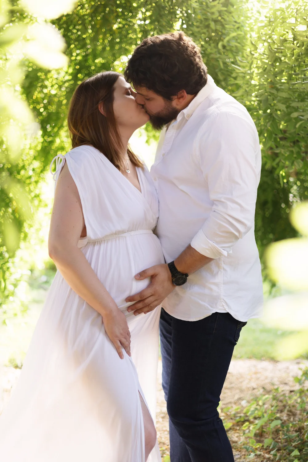Couple s’embrassant dans un jardin, la femme enceinte en robe blanche.