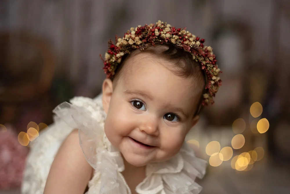 Bébé souriante avec une couronne de fleurs, en gros plan.