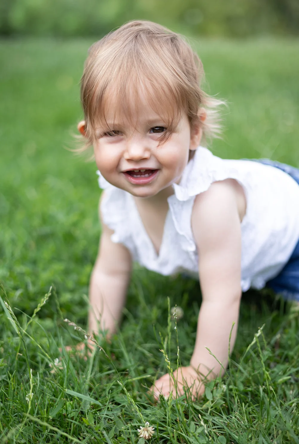Bébé à quatre pattes dans l’herbe, souriant.
