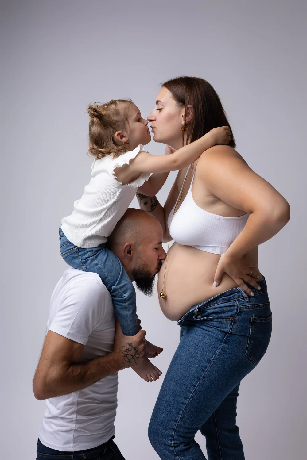 Famille en studio, l’enfant sur les épaules de papa embrassant maman.