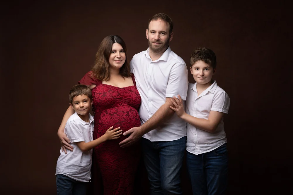 Famille de quatre en studio, la maman enceinte en robe bordeaux.