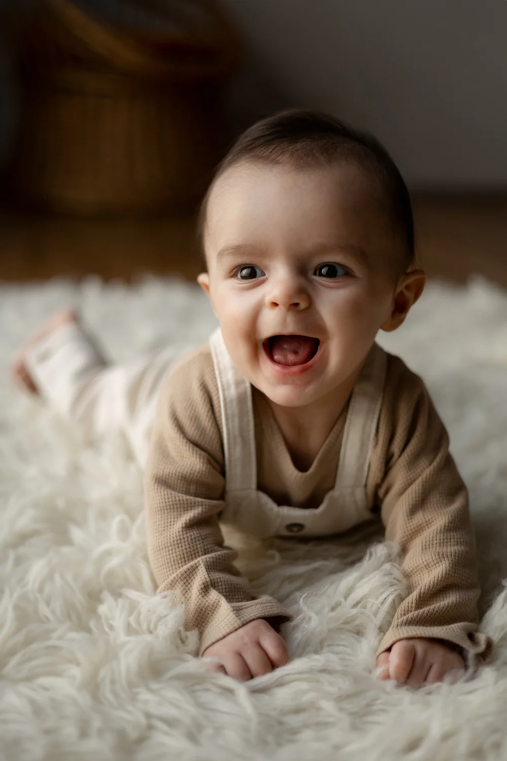 Bébé riant en tenue beige allongé sur une fourrure.