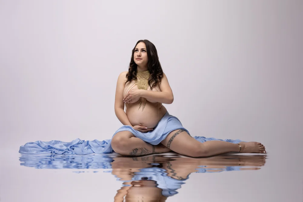 Femme enceinte assise avec un voile bleu et son reflet.