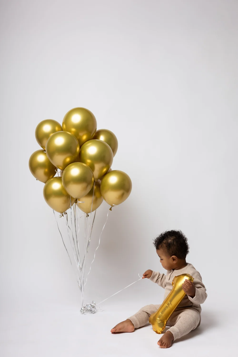 Bébé assis avec un ballon « 1 » sous un bouquet de ballons dorés.
