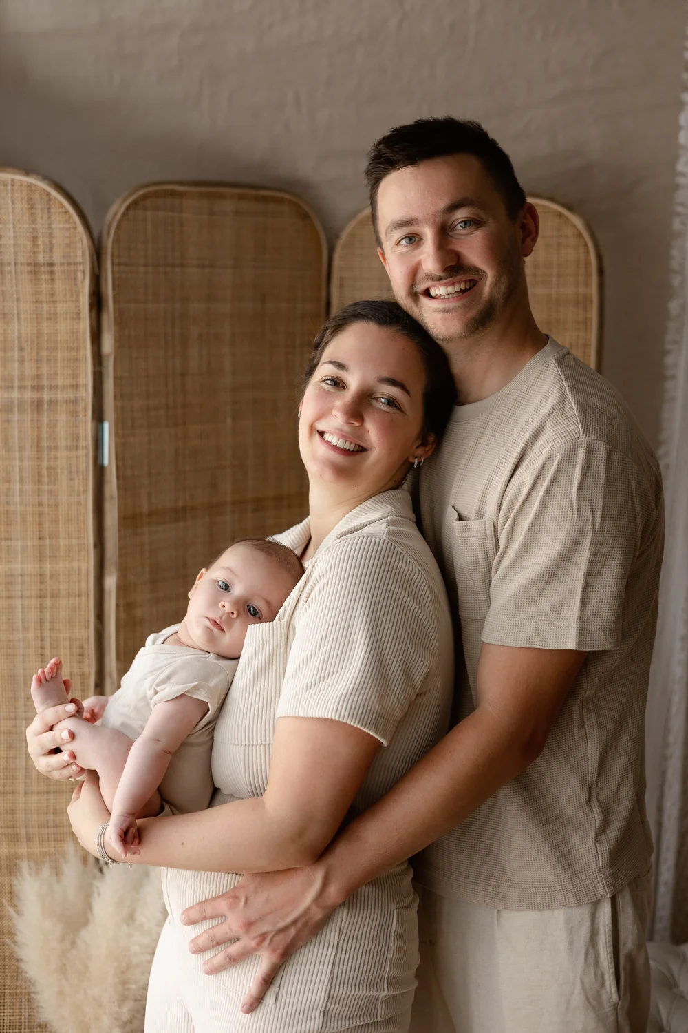 Parents souriants tenant leur nouveau-né devant un paravent.