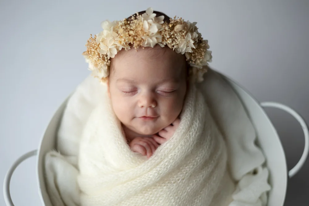 Nouveau-né endormi avec une couronne de fleurs dans un seau blanc.