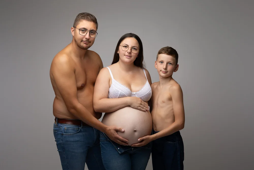 Parents et leur fils en studio, torse nu, mains sur le ventre.