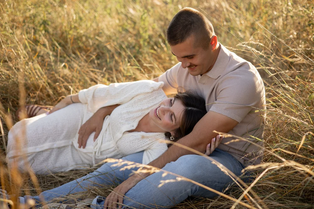 Femme enceinte blottie contre son conjoint dans les hautes herbes dorées.