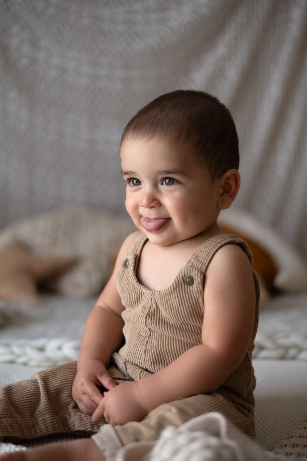 Bébé souriant en salopette beige assis en studio.