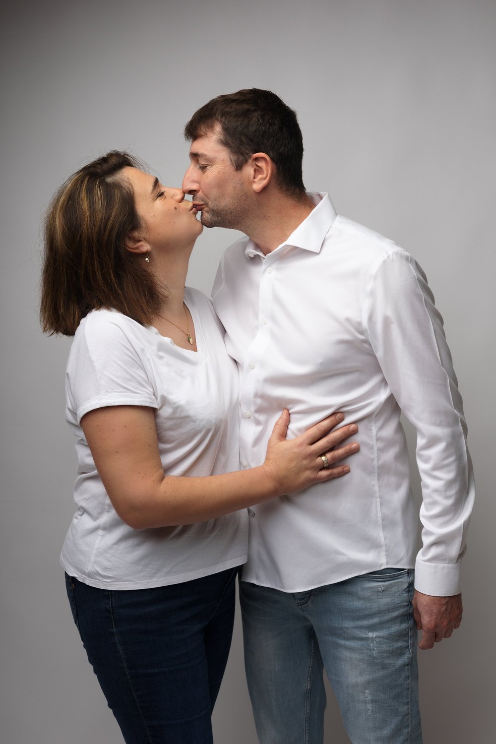 Couple s’embrassant en studio, sur fond gris.