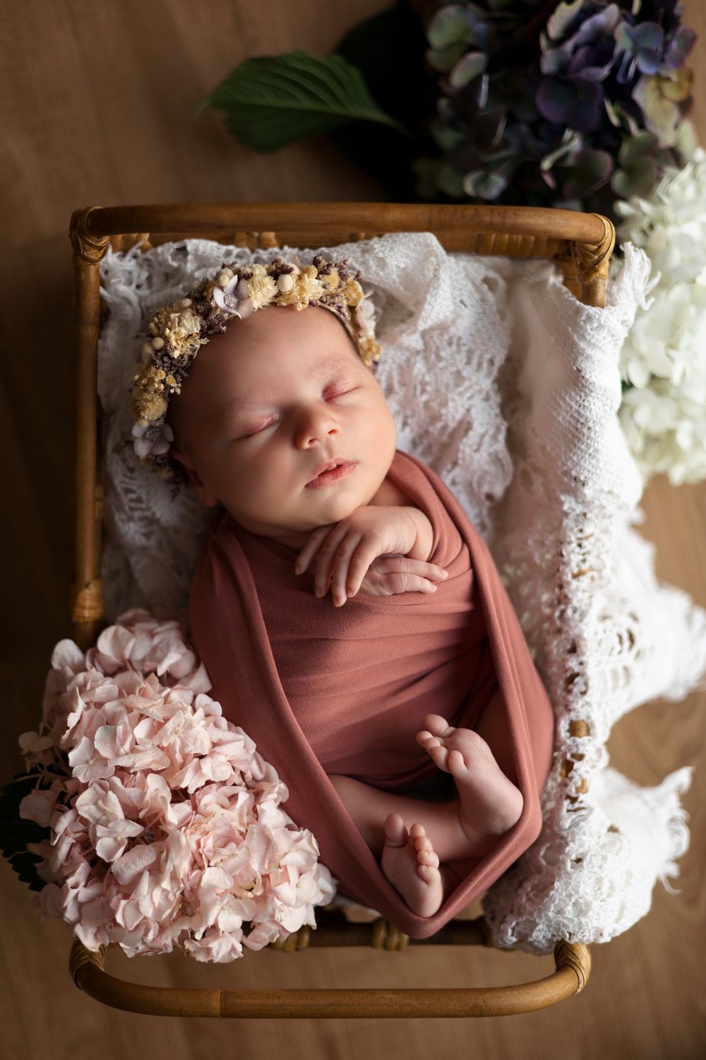Nouveau-né emmailloté de vieux rose, couronne de fleurs, dans un panier fleuri.