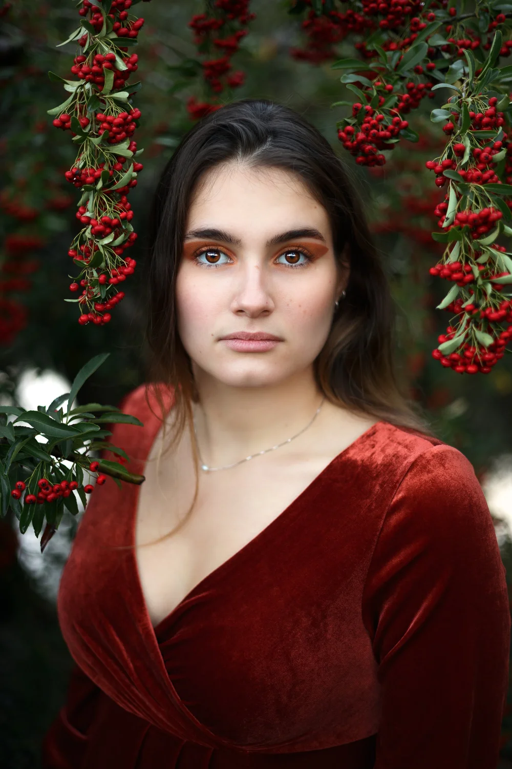 Portrait d’une femme en robe de velours rouge sous des baies rouges.