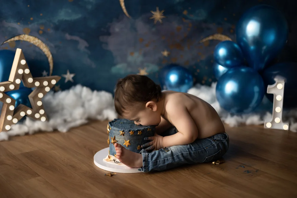 Bébé penché sur son gâteau devant un décor de ciel étoilé bleu.
