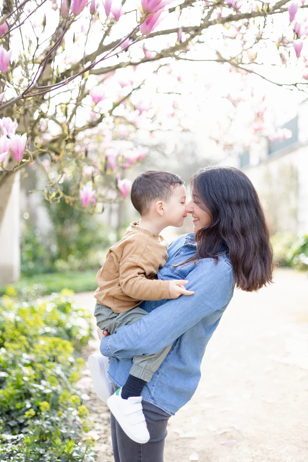 Maman et son petit garçon nez contre nez sous un magnolia en fleurs.