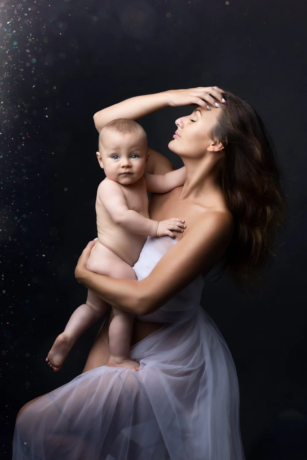 Maman tenant son bébé nu contre elle, sur fond sombre.