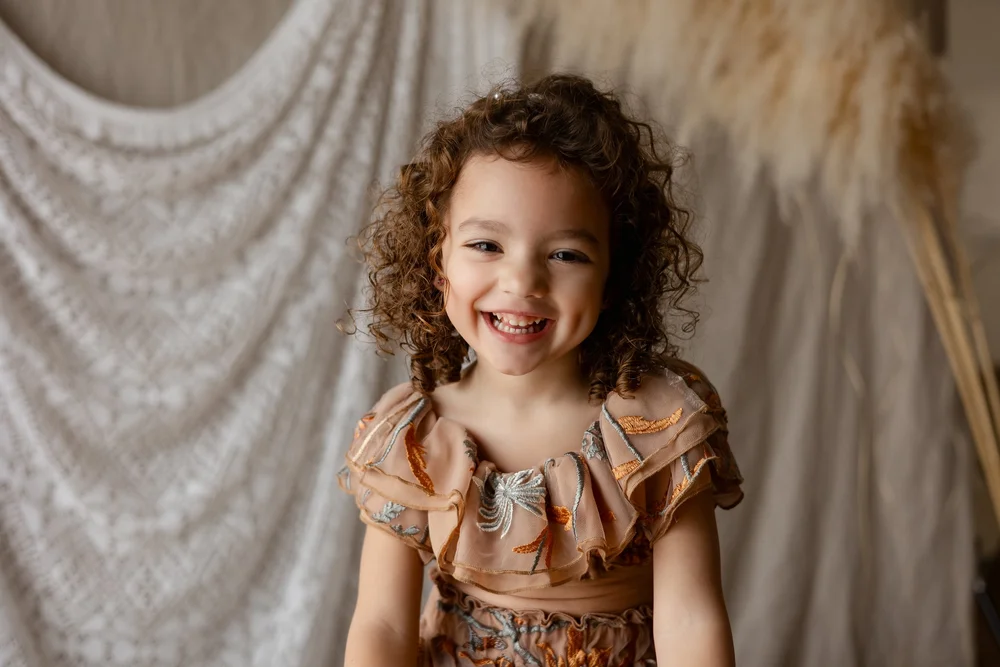 Petite fille aux cheveux bouclés éclatant de rire, en robe fleurie, en studio.