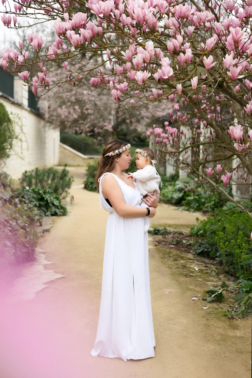 Maman en robe blanche avec son bébé sous un magnolia en fleurs.