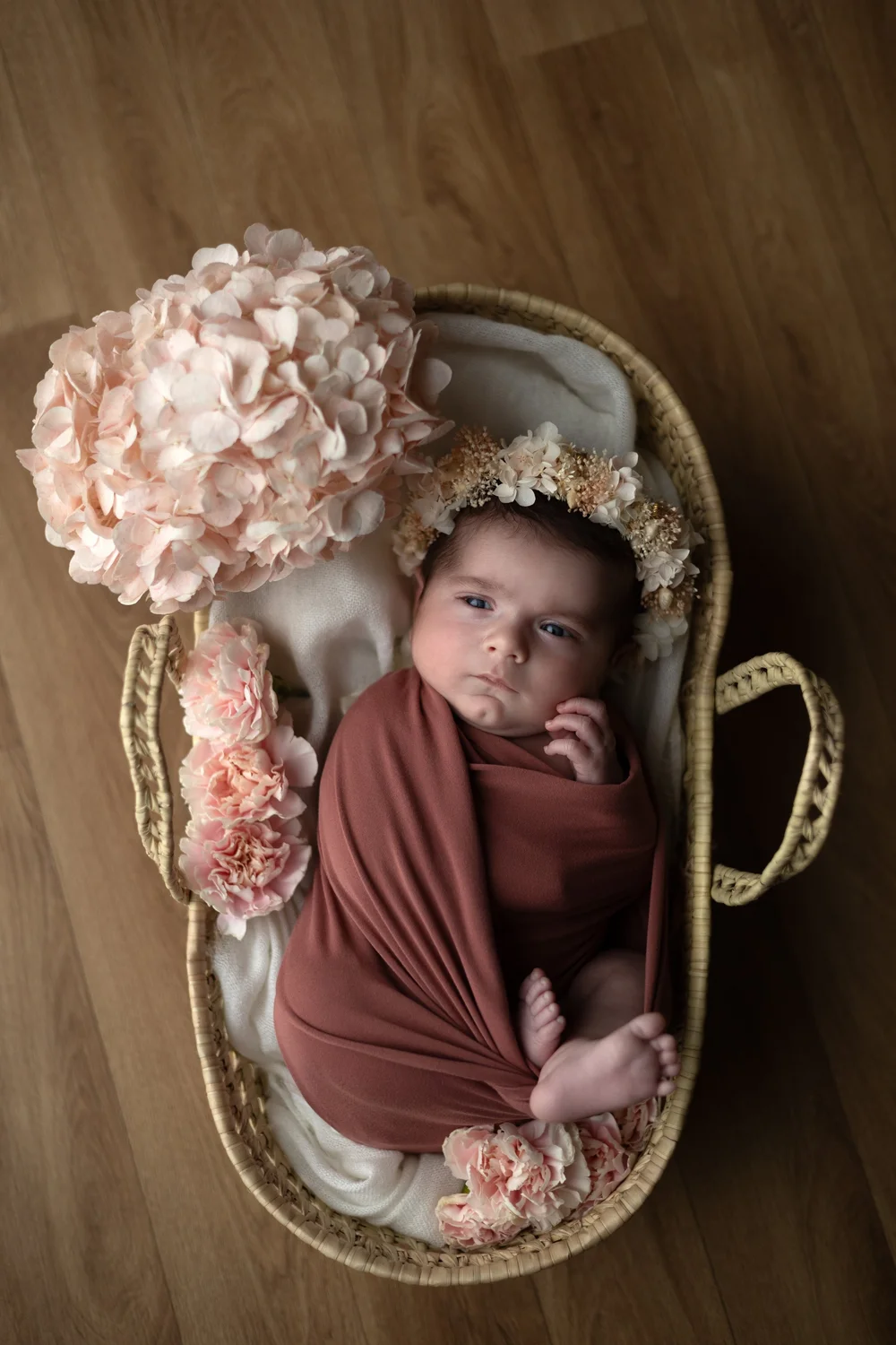 Nouveau-né emmailloté de rose dans un couffin en osier avec des fleurs.