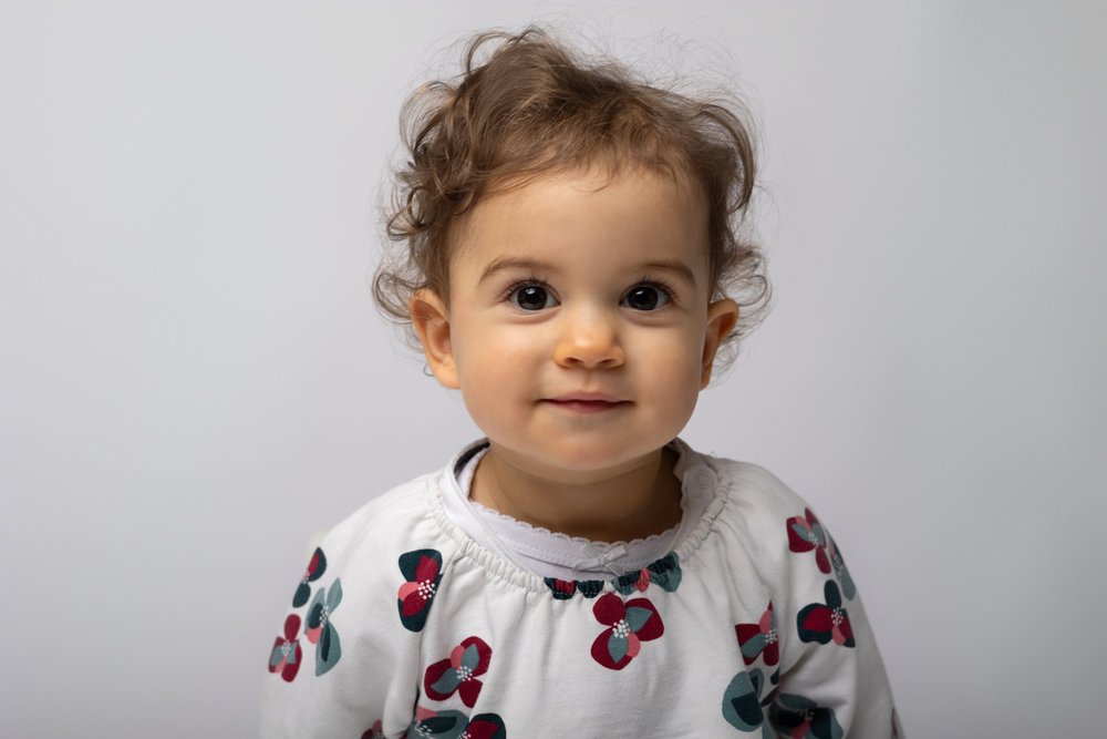 Portrait d’un bébé en haut à motifs de cerises, sur fond clair.