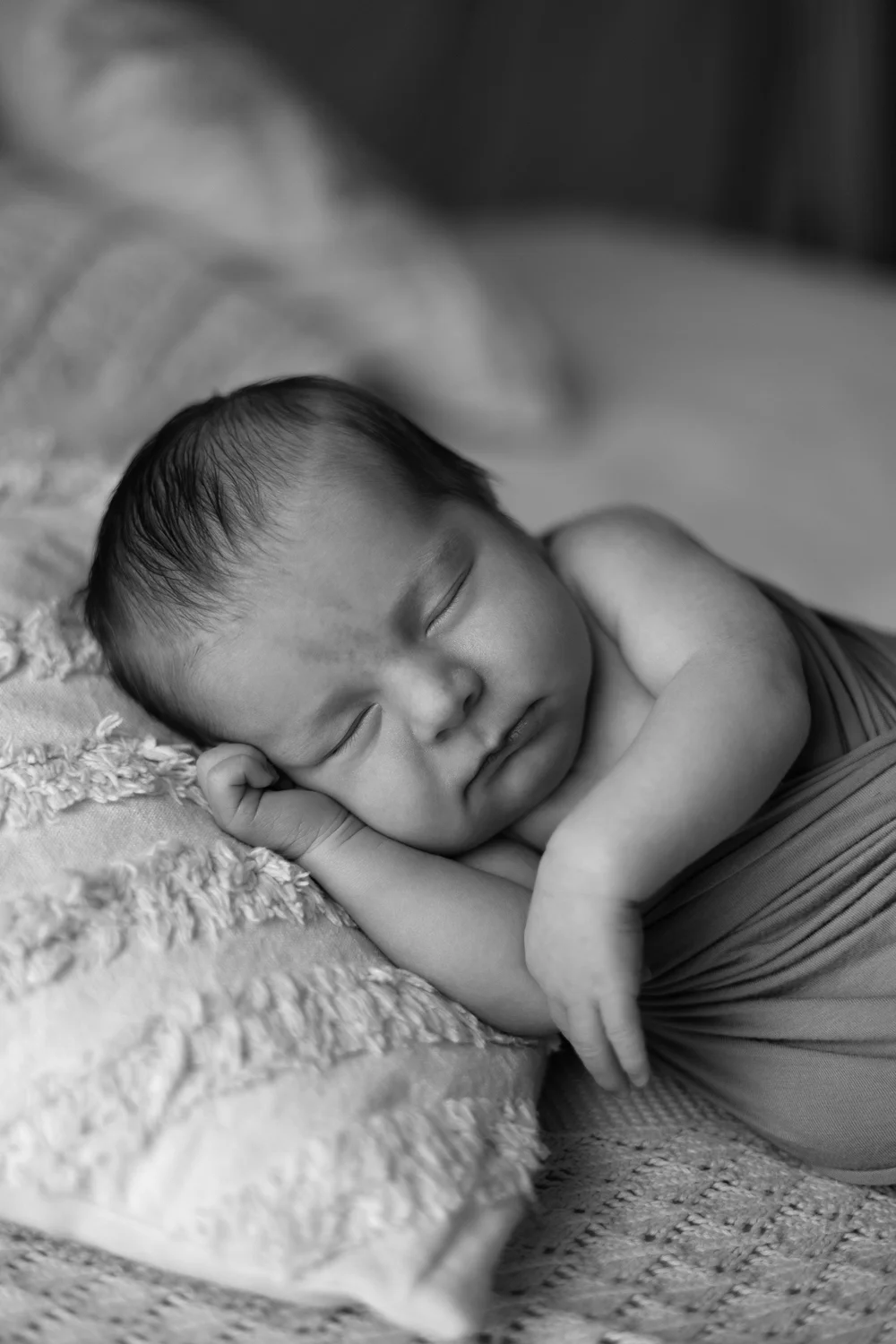 Nouveau-né endormi sur un lit, en noir et blanc.