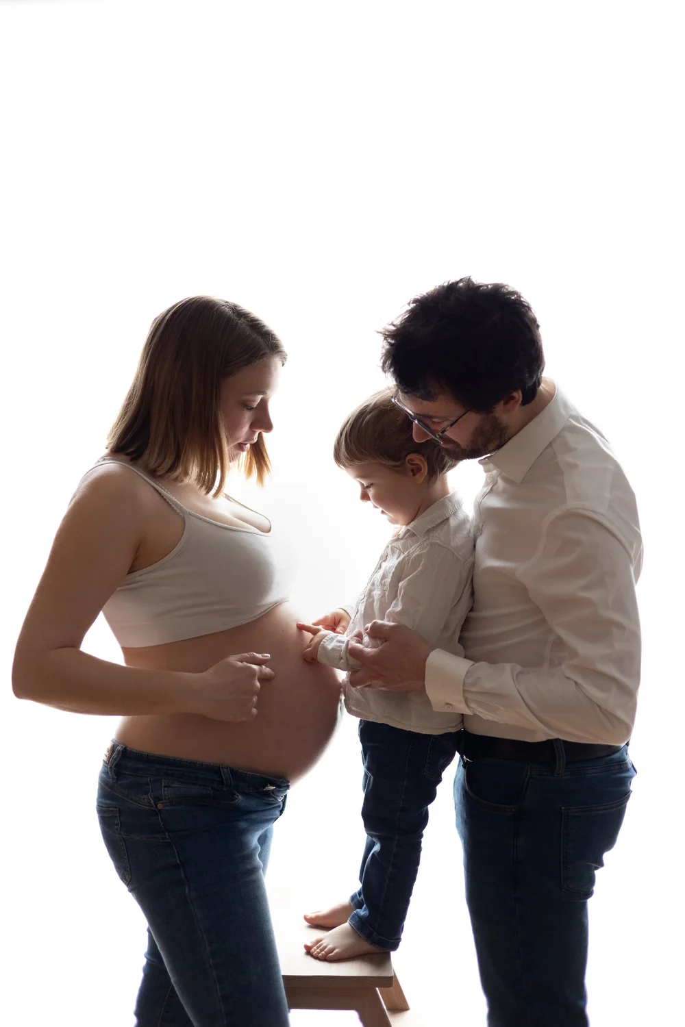 Parents et jeune enfant regardant le ventre de maman, en contre-jour.
