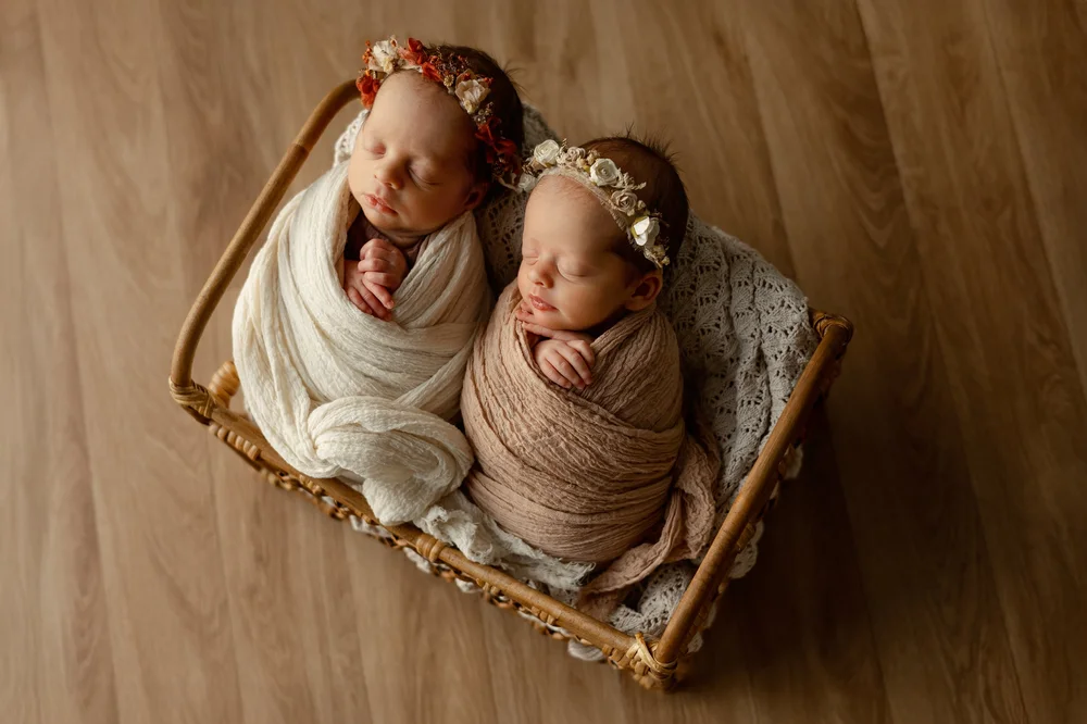 Deux nouveau-nés emmaillotés côte à côte dans un petit lit en bois.