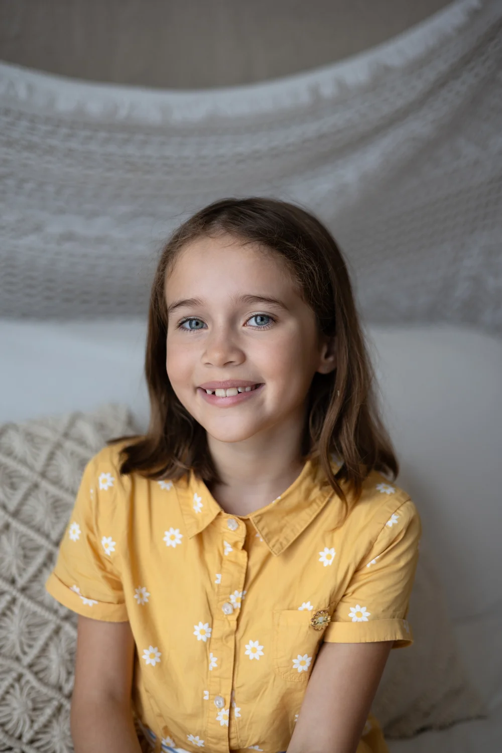 Fillette souriante en chemise jaune, sur fond clair.