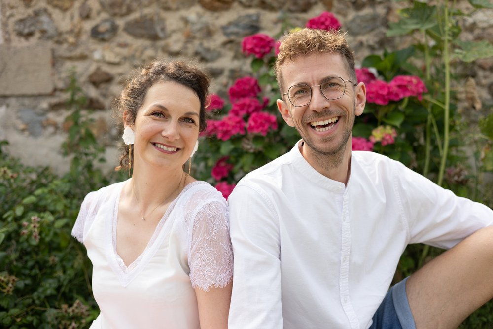 Couple souriant devant un rosier rouge.