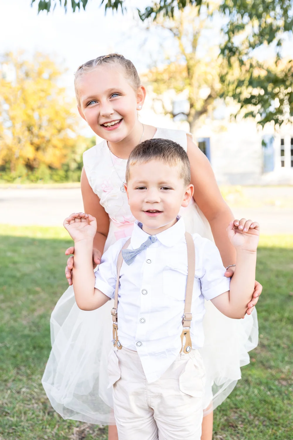 Petite fille et petit garçon souriants, en tenue de cérémonie.