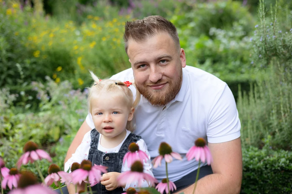 Papa et son bébé devant des fleurs roses, en extérieur.
