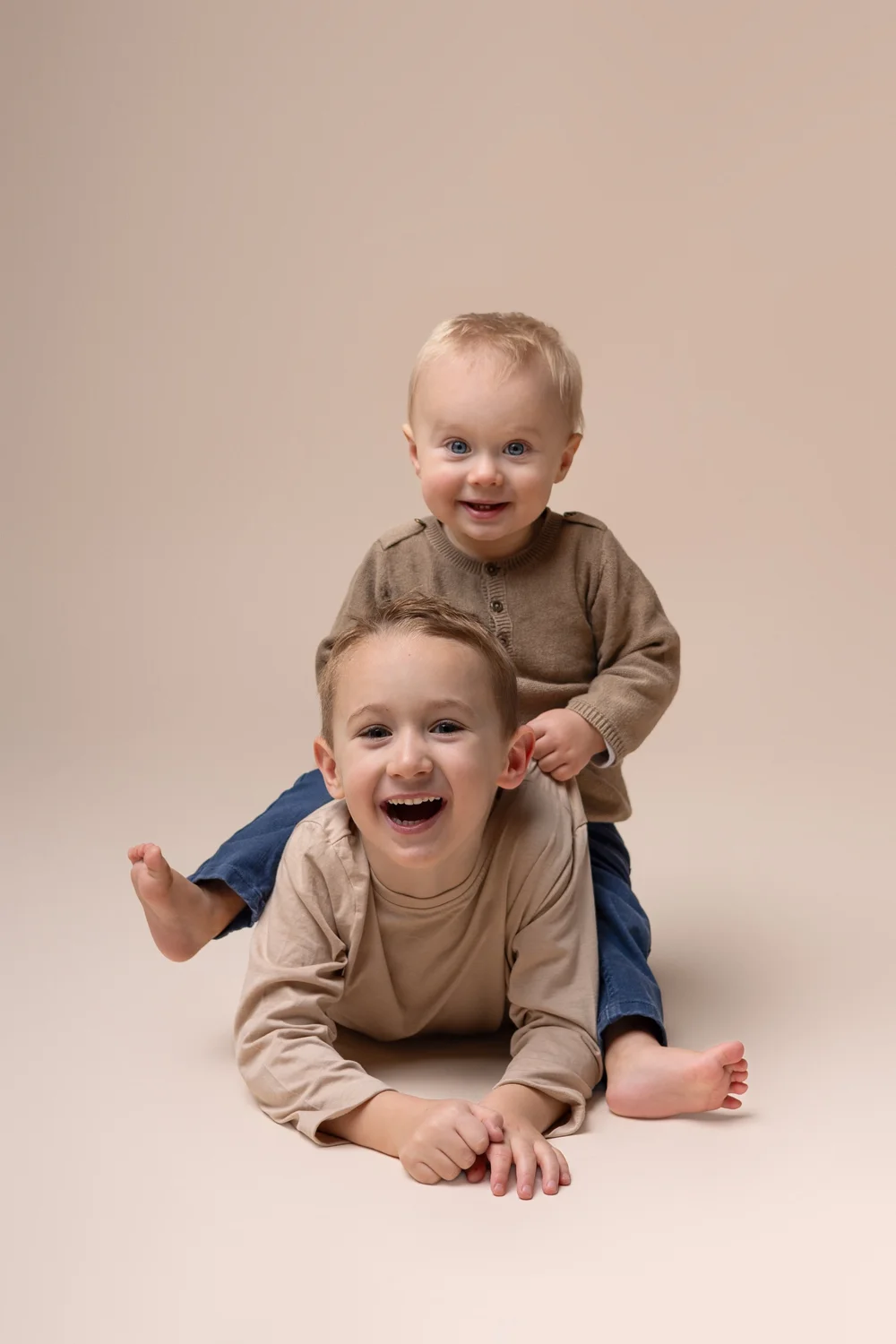 Deux frères rieurs l’un sur l’autre, en studio sur fond beige.