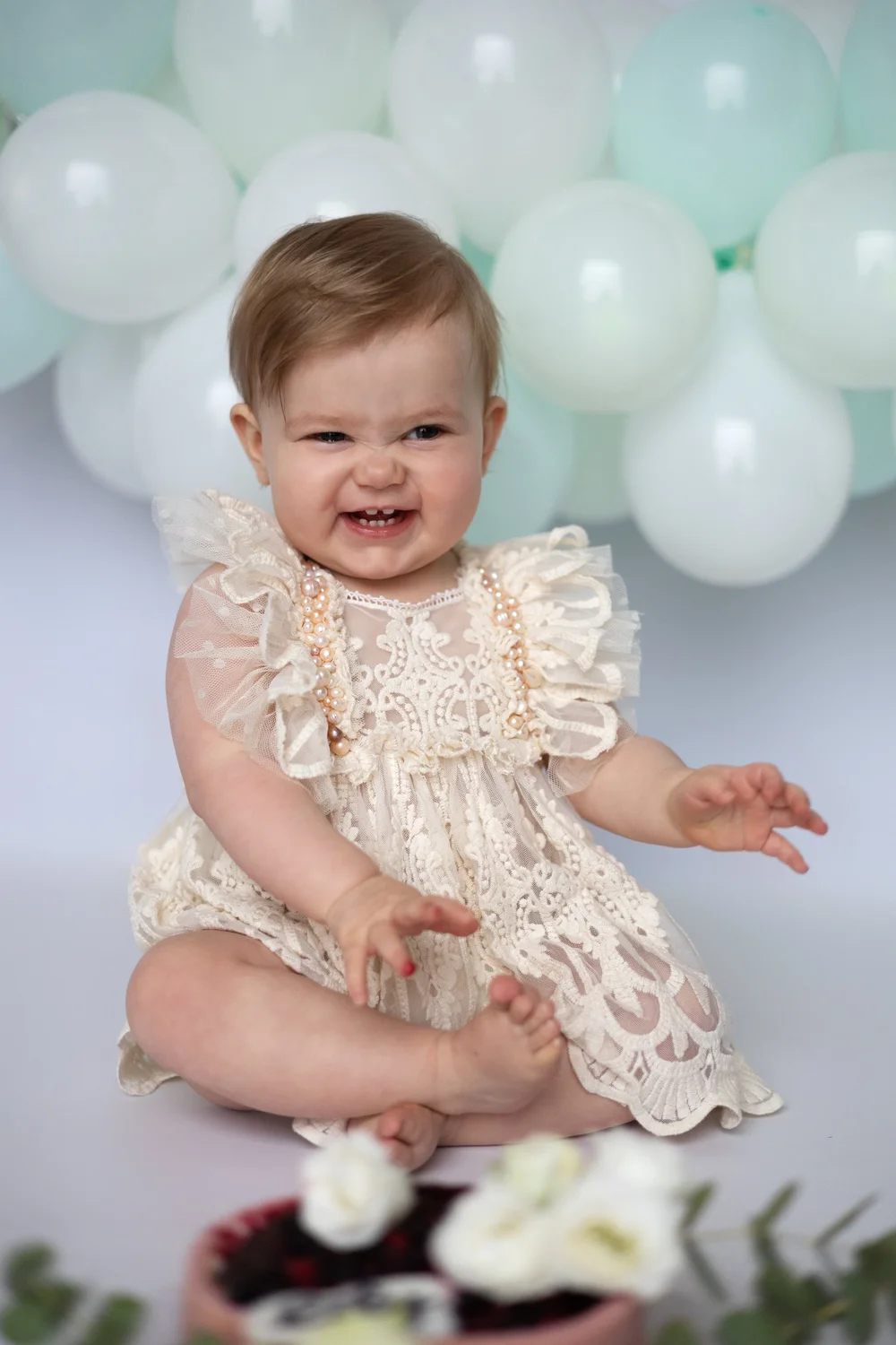 Bébé en robe de dentelle devant des ballons vert d’eau.