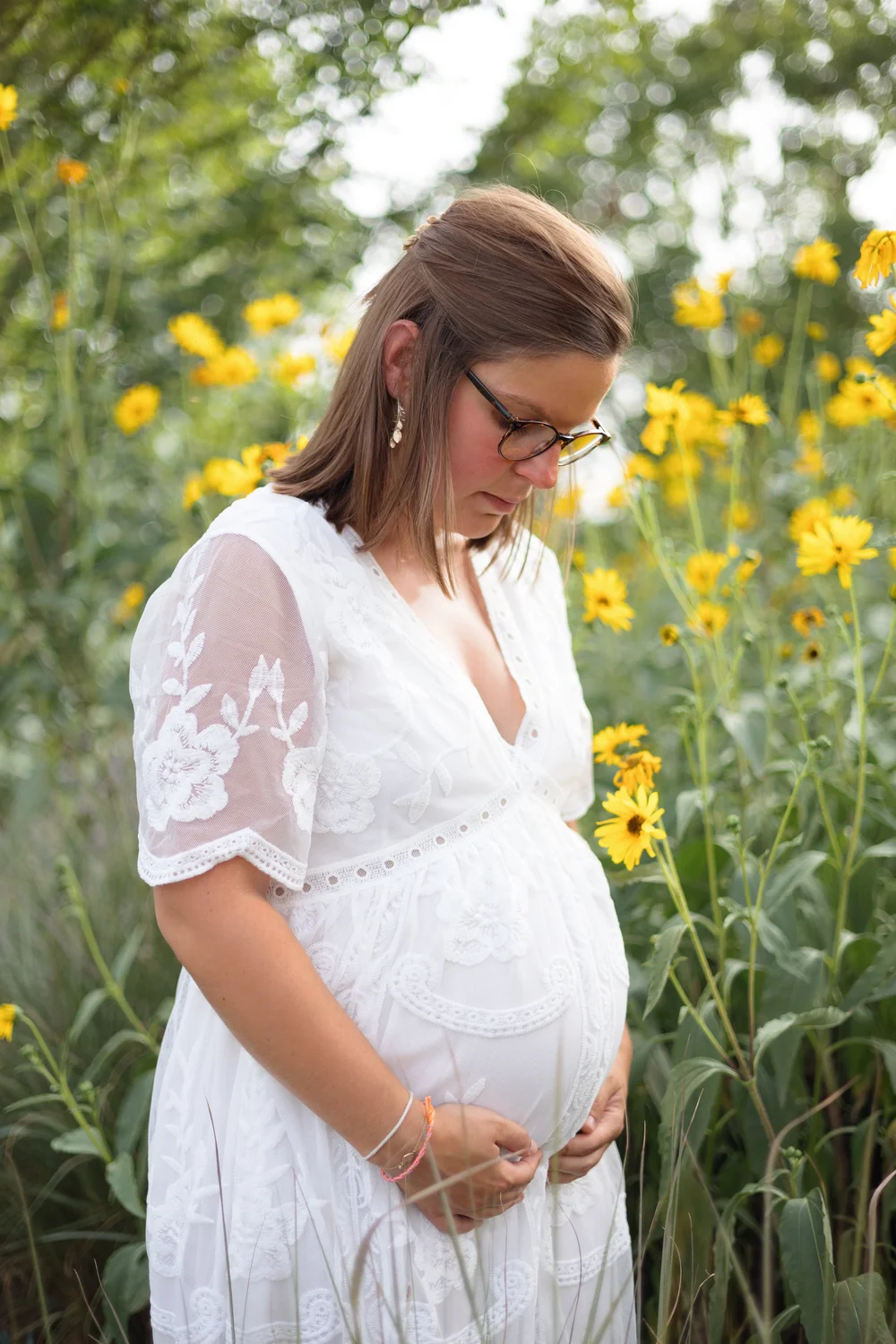 Femme enceinte en robe de dentelle blanche parmi des fleurs jaunes.