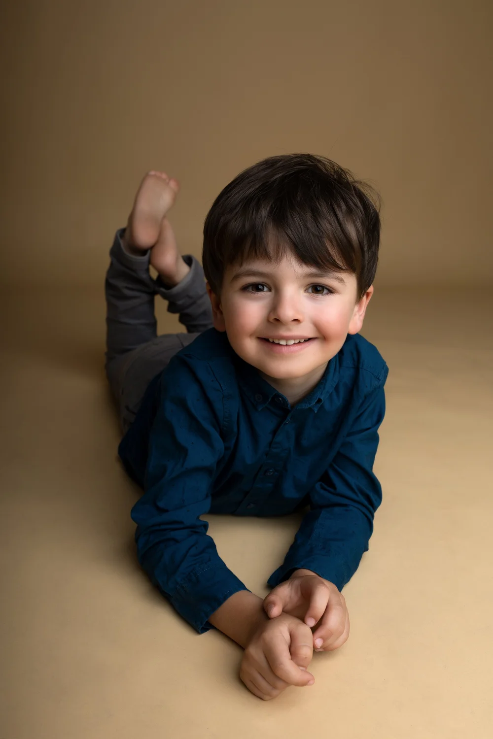 Petit garçon allongé sur le ventre en chemise bleue, sur fond beige.