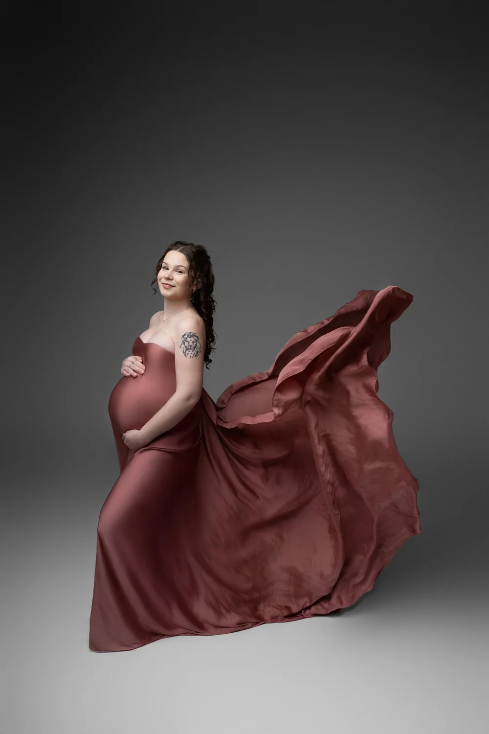 Femme enceinte en robe rouge dont le voile flotte, sur fond gris.