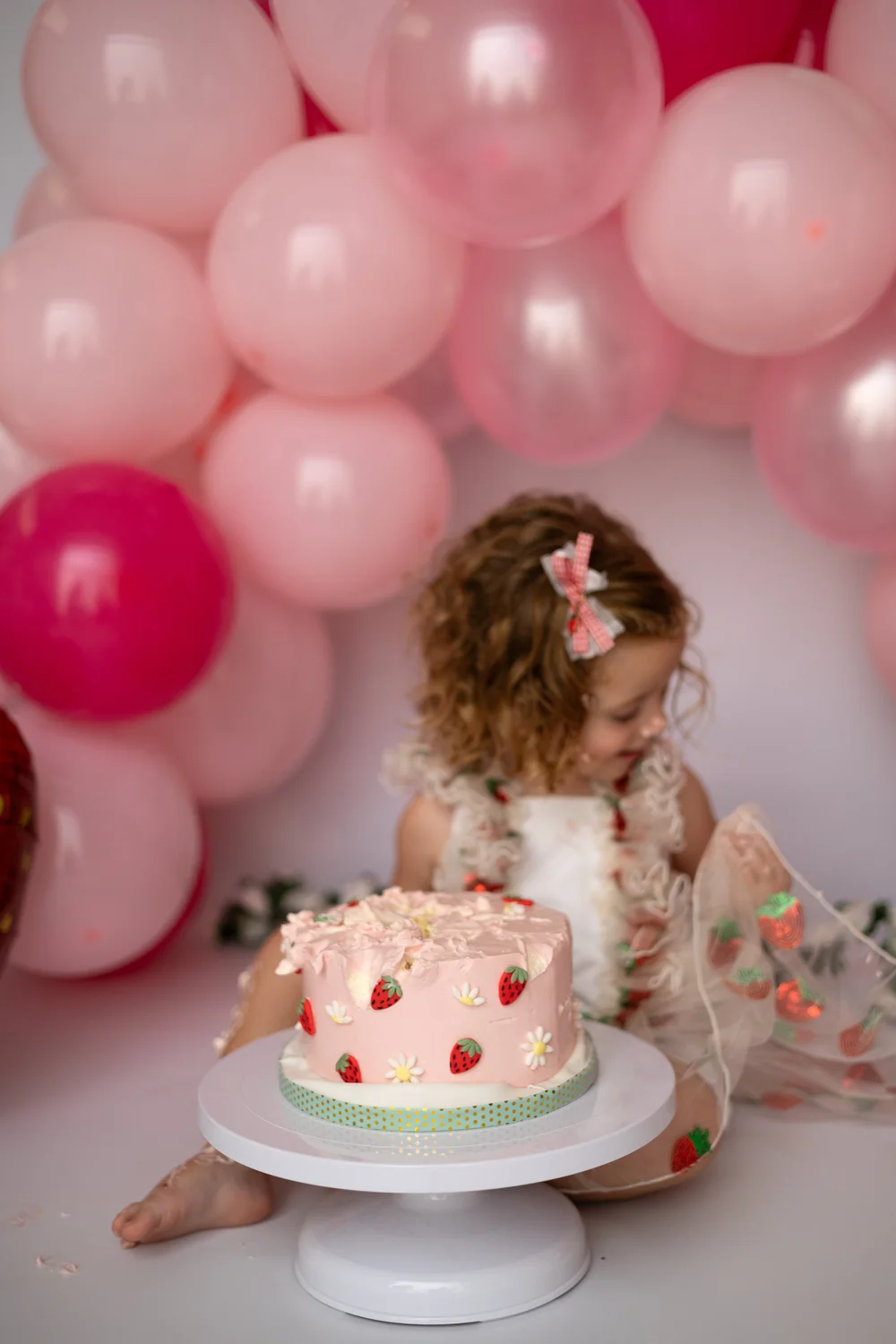 Petite fille devant son gâteau sous une arche de ballons roses.