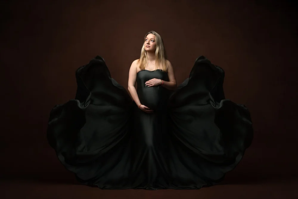 Femme enceinte en robe noire qui vole, en studio.