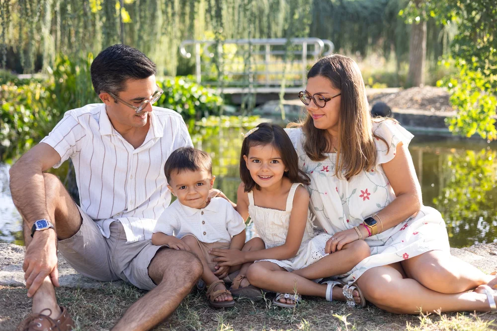 Famille assise dans l’herbe au bord d’un étang, avec leurs trois enfants.